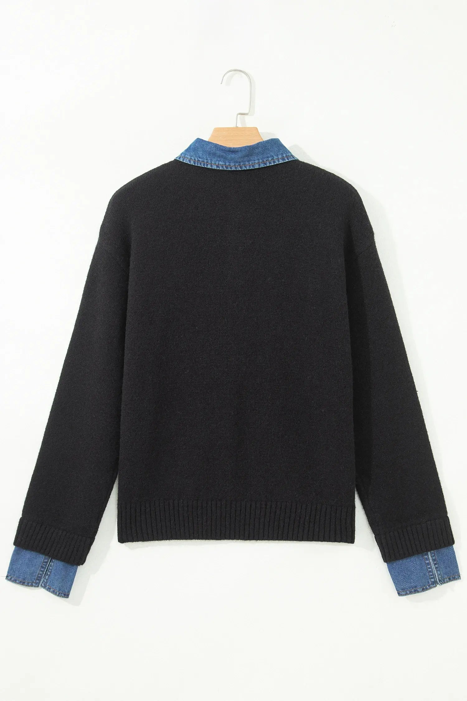 A black knit sweater with contrasting blue denim trim at the collar and cuffs, hanging on a wooden hanger against a plain white background.
