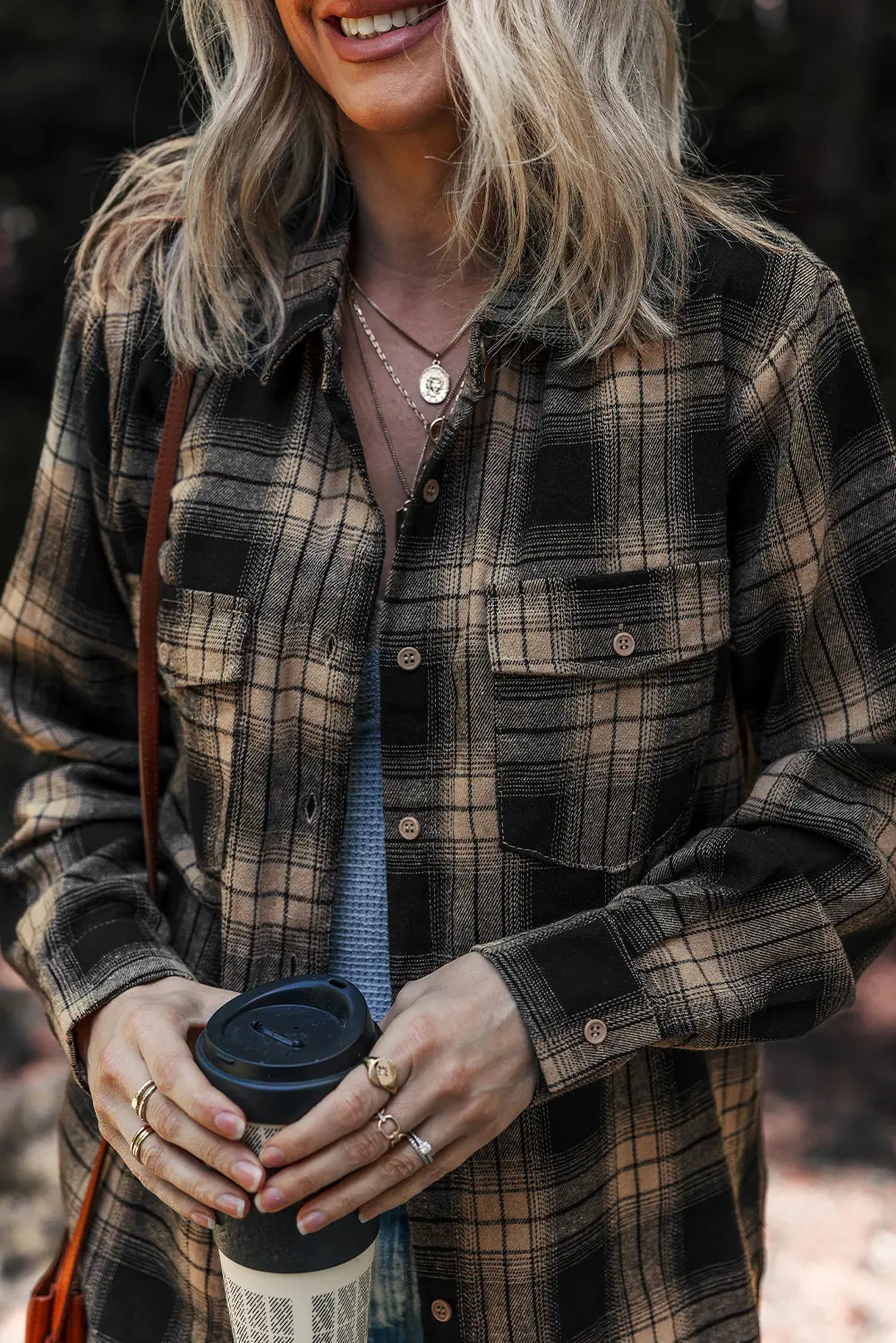Person wearing a plaid shirt holding a coffee cup outdoors