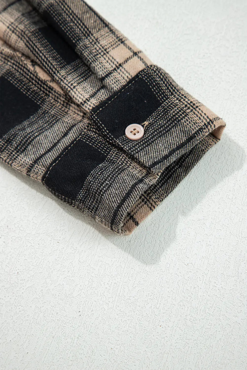 Folded plaid shirt with a button on a light gray background