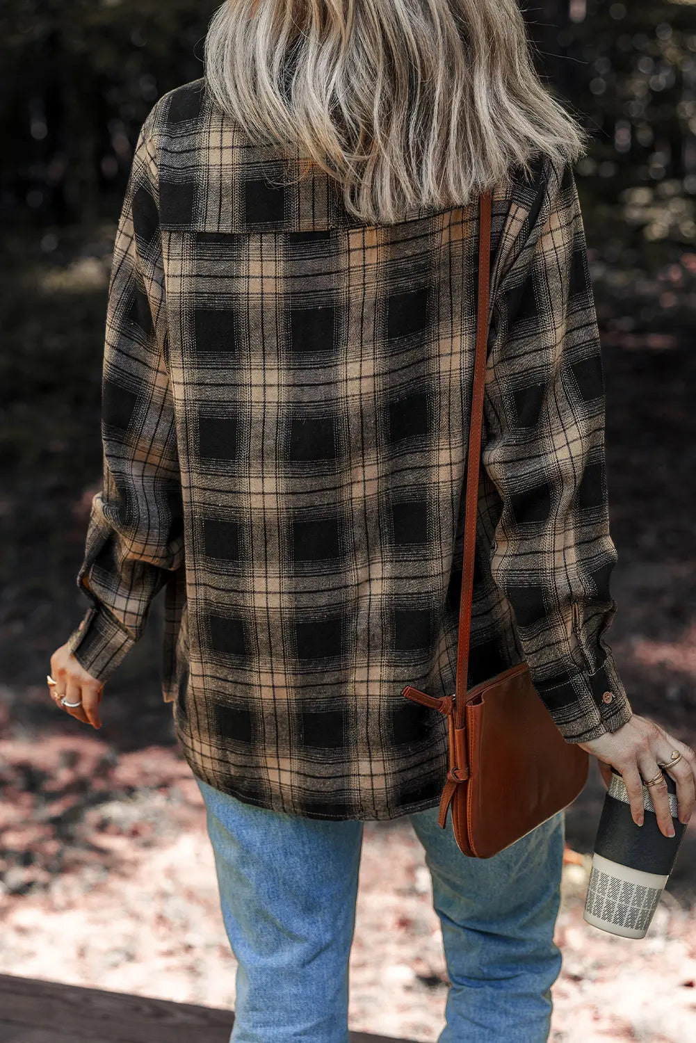 Person wearing a plaid shirt and blue jeans with a brown leather bag outdoors.