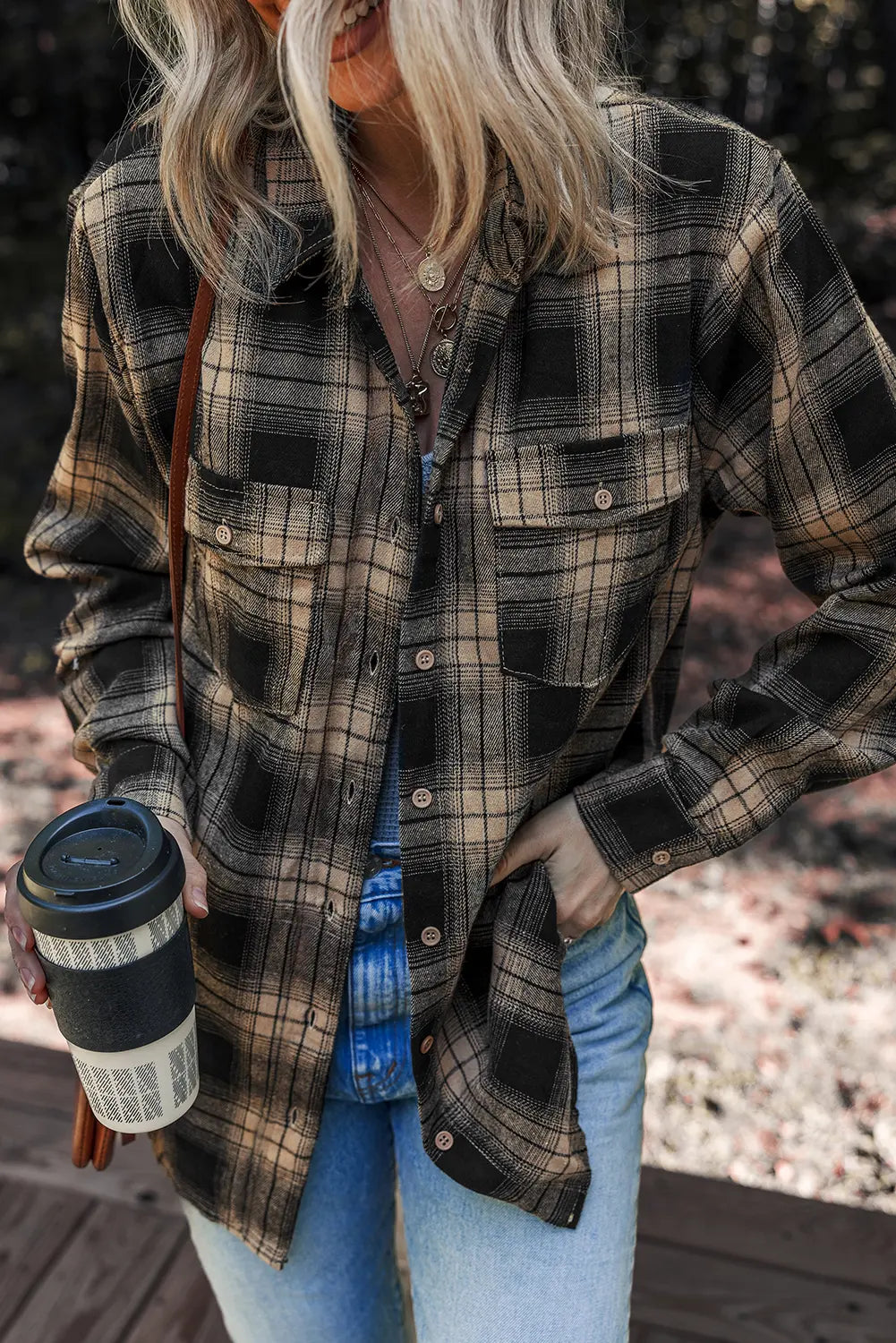 Person wearing a plaid shirt holding a coffee cup outdoors
