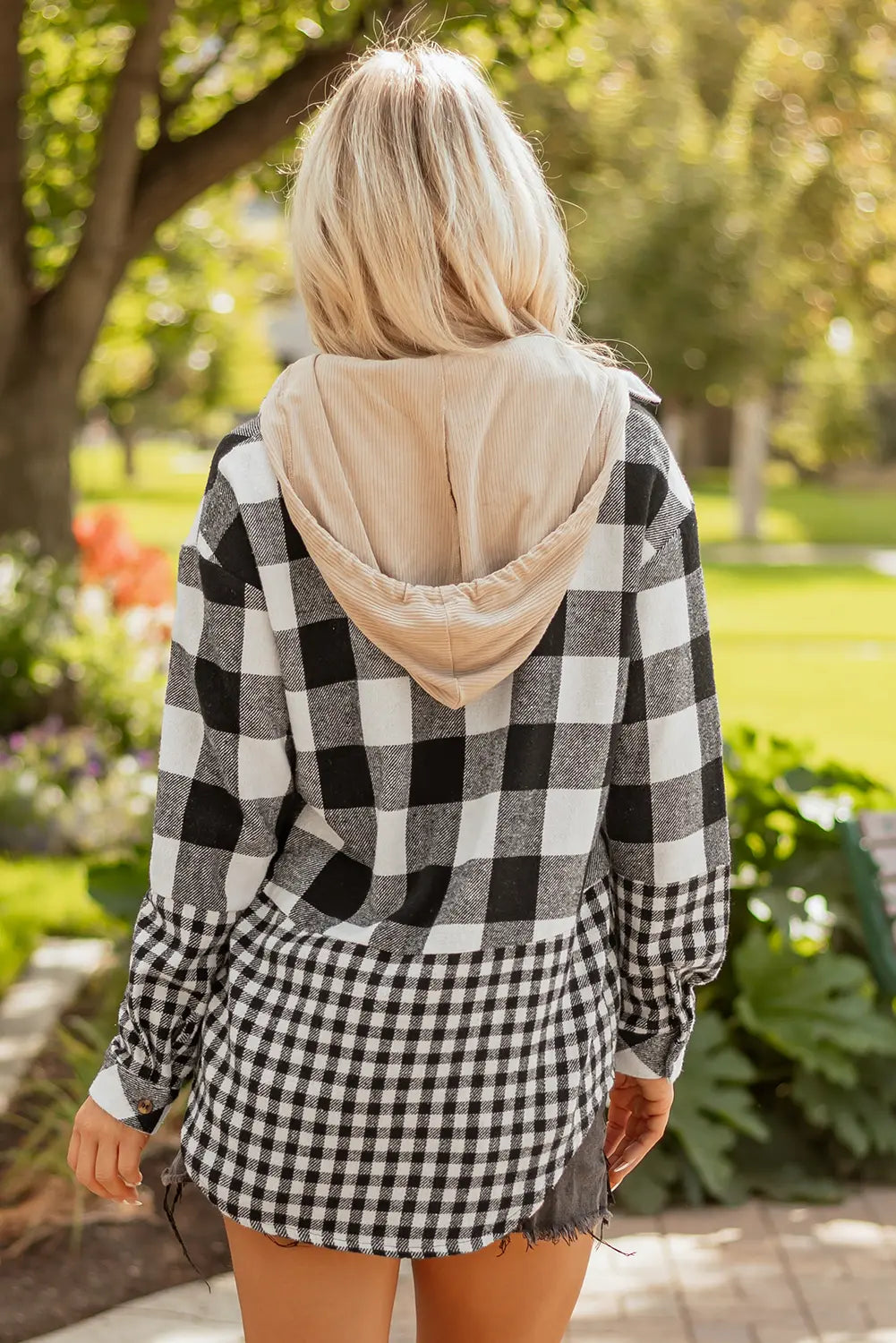 Person wearing a black and white checkered shirt with a beige hood in an outdoor setting.