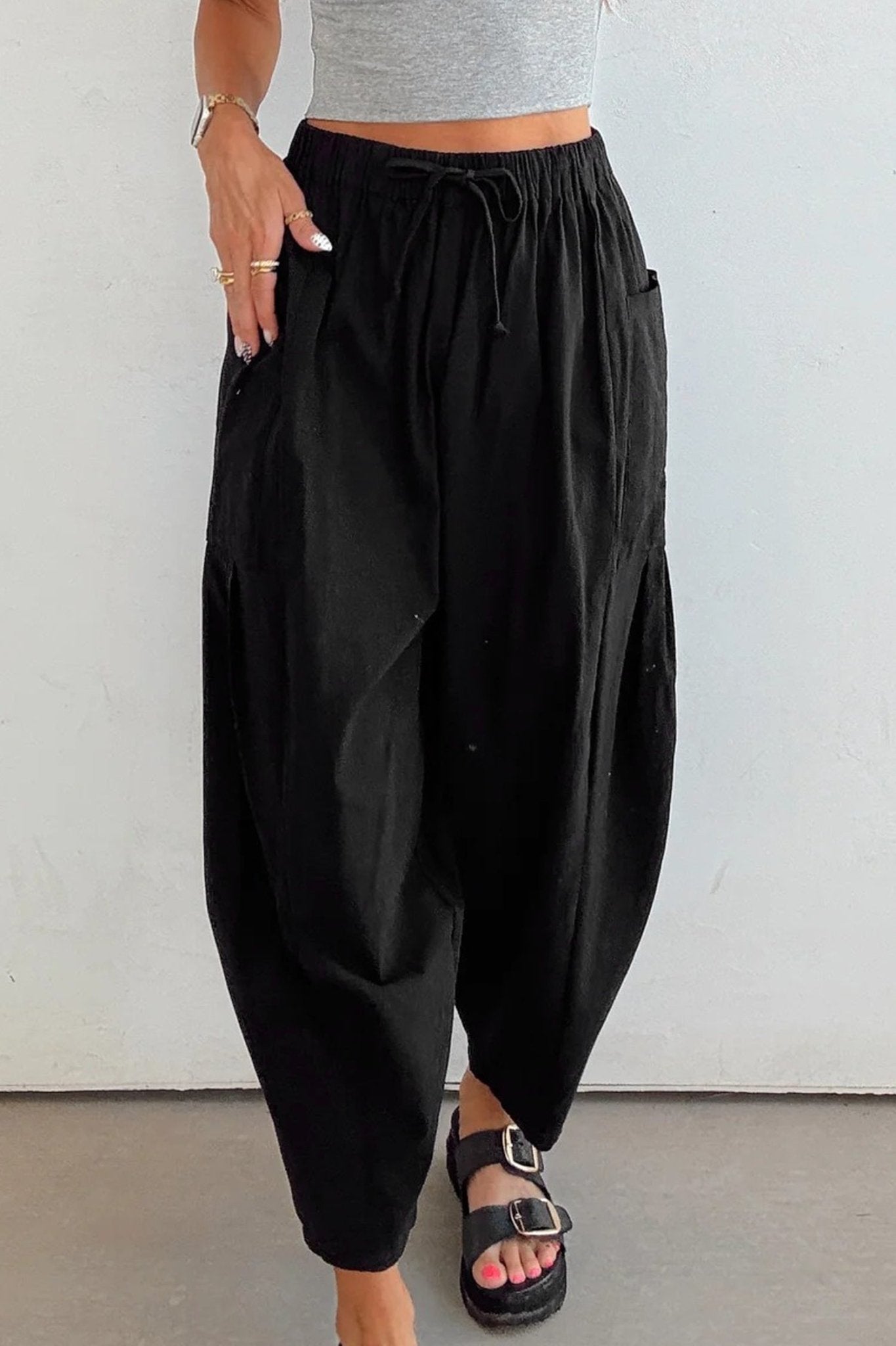 Person wearing black harem pants and a gray top against a white background