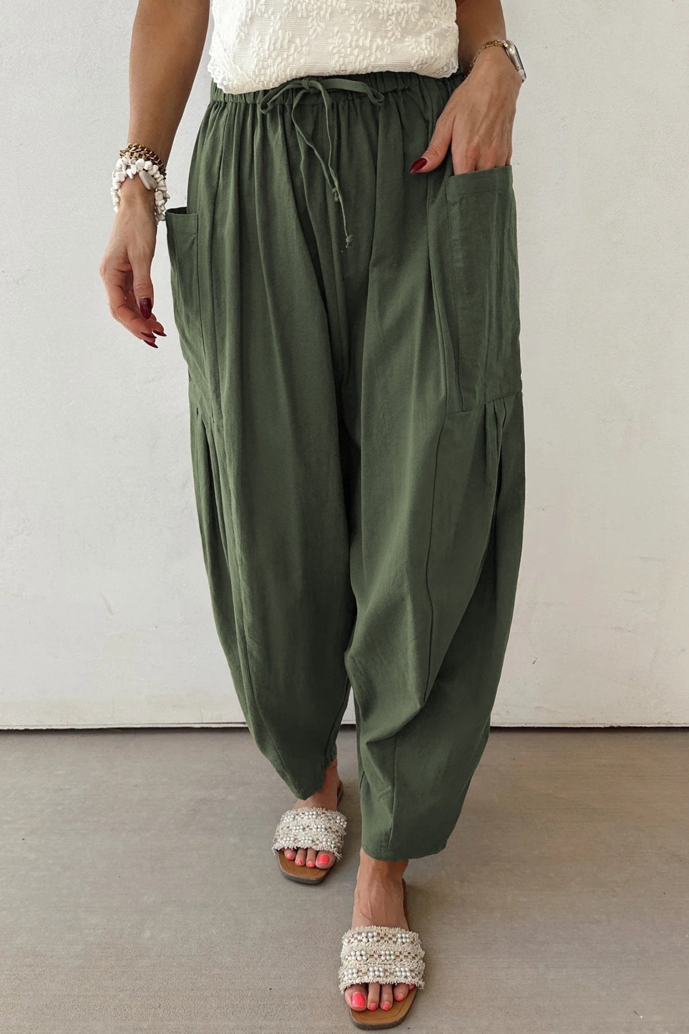 Person wearing olive green wide-leg pants with a white top and sandals on a neutral background