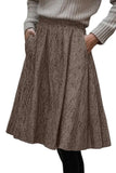 A brown and beige textured herringbone skirt with side pockets, worn by a model in a gray ribbed sweater against a white background.
