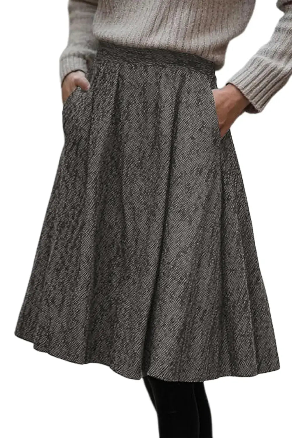 A gray and black herringbone patterned pleated skirt with side pockets, worn by a model in a ribbed beige sweater.