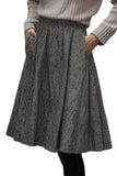 A gray and black herringbone patterned pleated skirt with side pockets, worn by a model in a ribbed beige sweater.