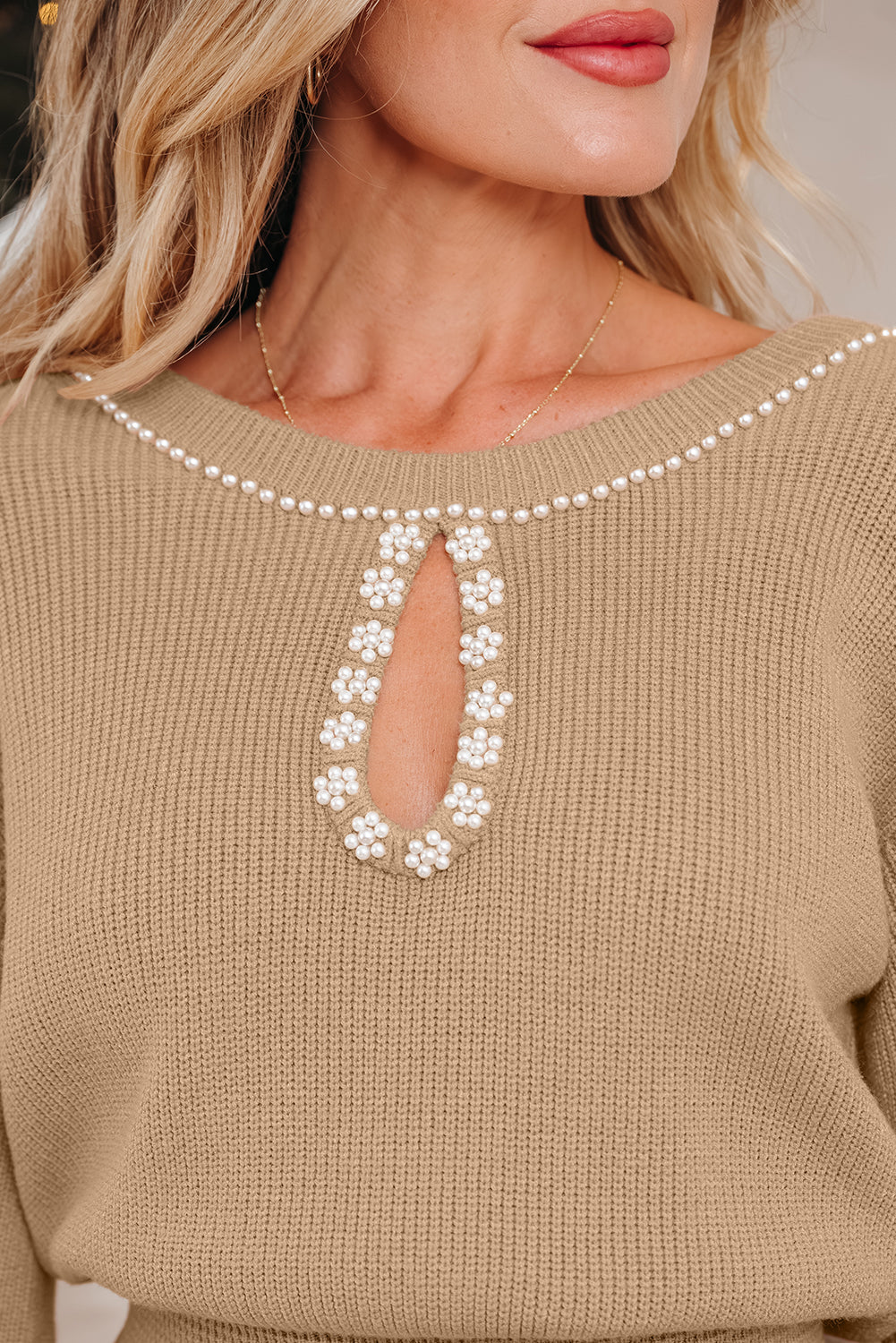 Beige sweater with a decorative pearl and flower pattern on a neutral background