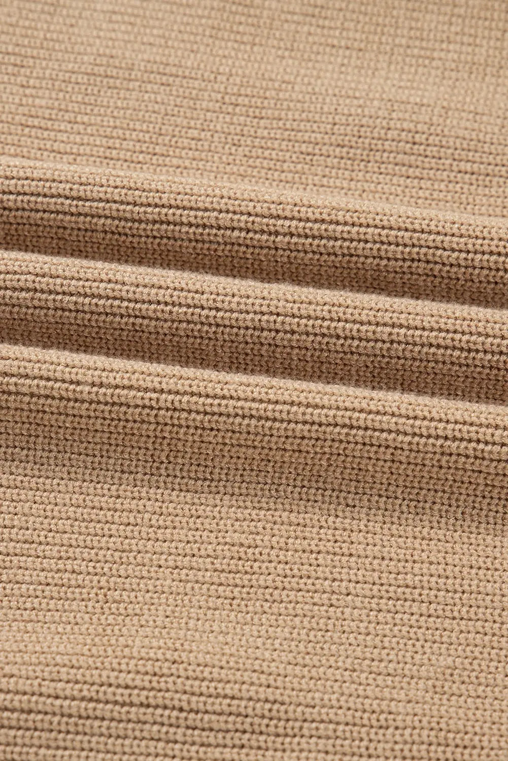 Close-up of a ribbed knit fabric in a warm tan or camel color, showing the detailed texture and folds.