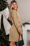 Woman in a beige dress standing in front of a decorated Christmas tree and fireplace.