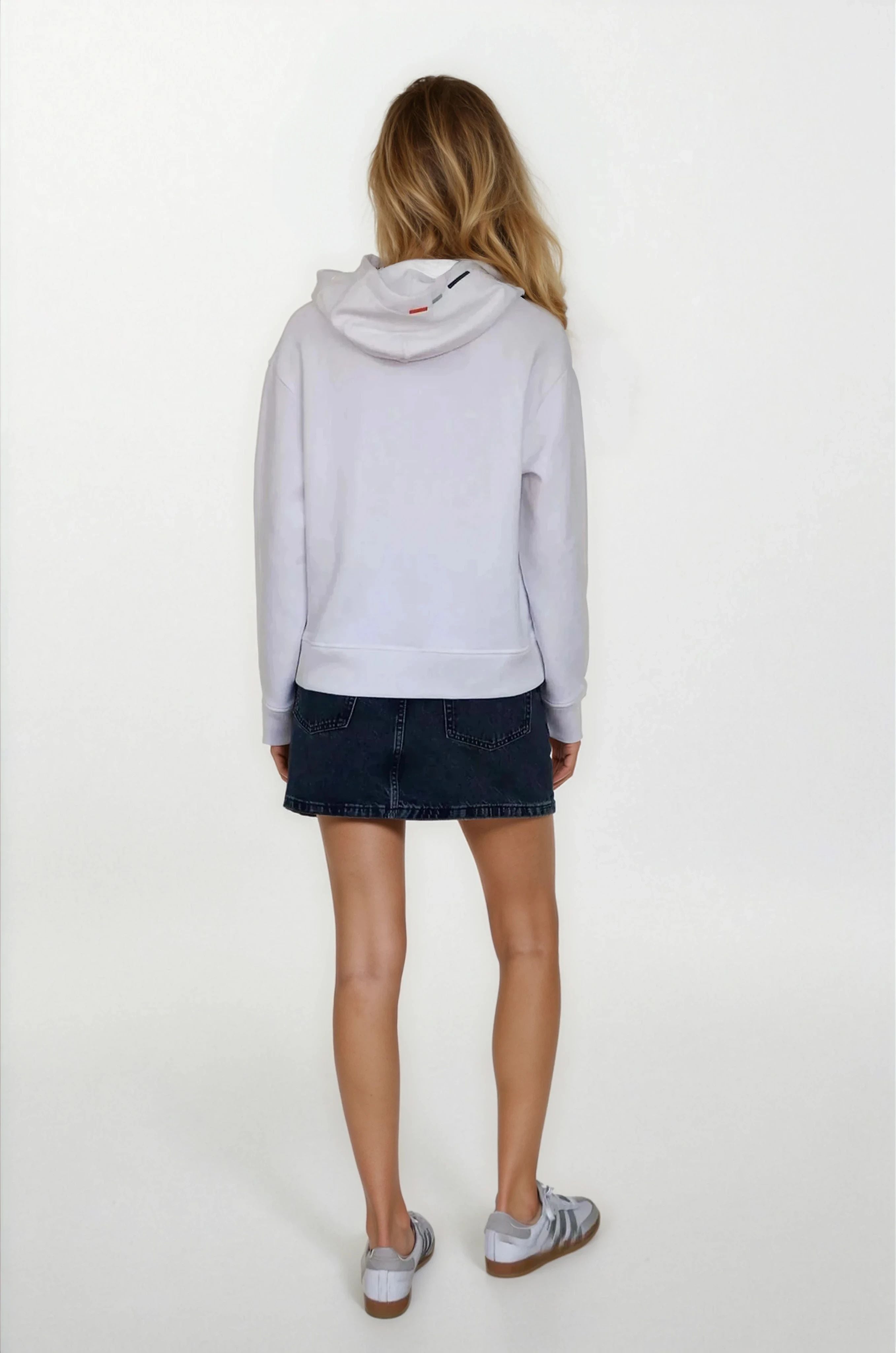 Person wearing a light gray hoodie and dark denim shorts on a white background