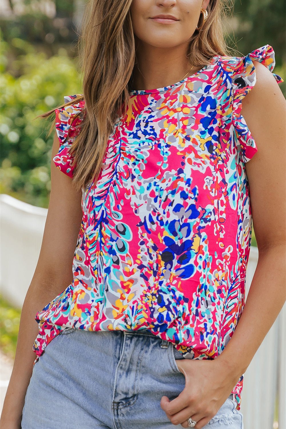 Woman wearing a colorful floral top with ruffled sleeves outdoors.