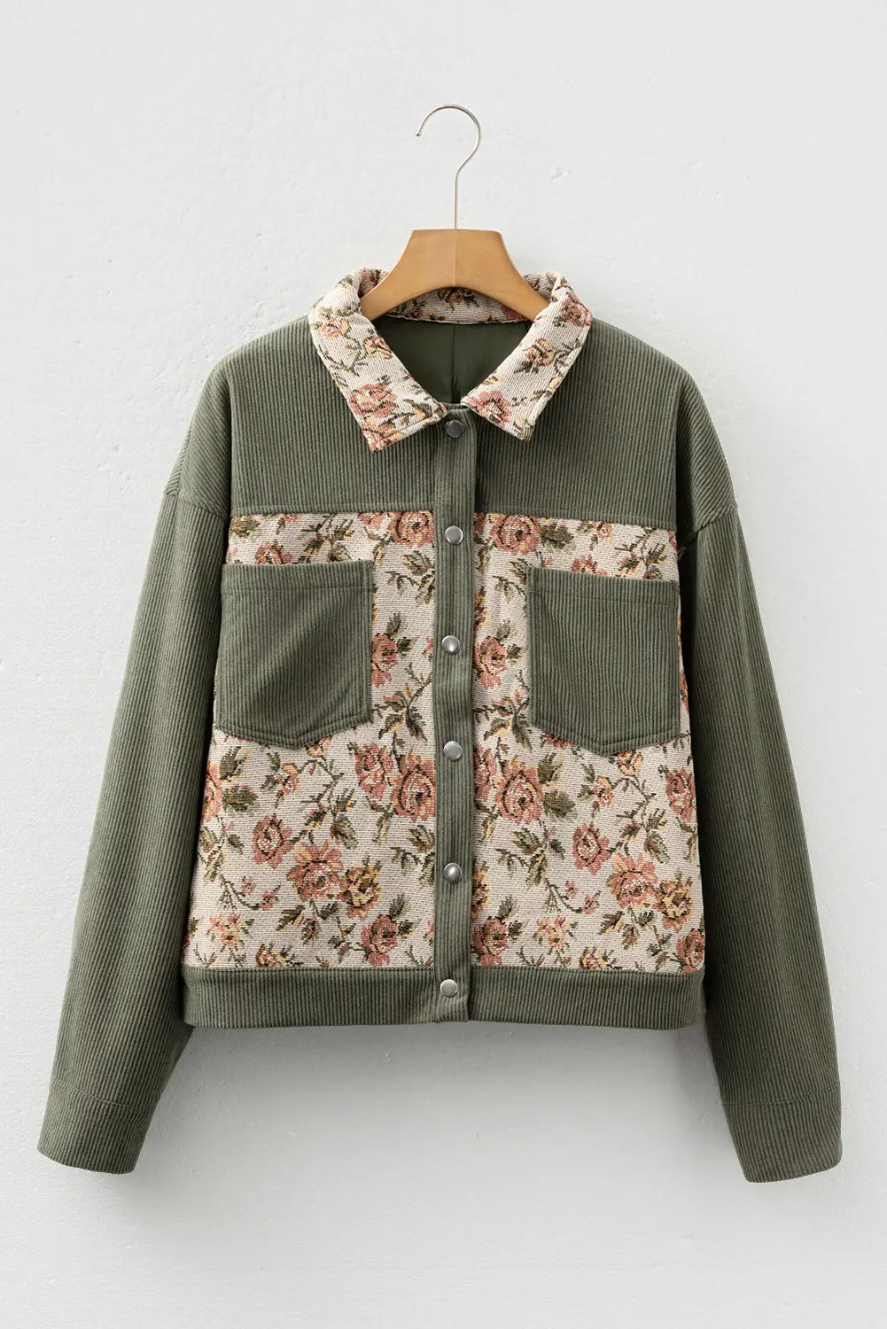 Green jacket with floral patterns on a wooden hanger against a white background