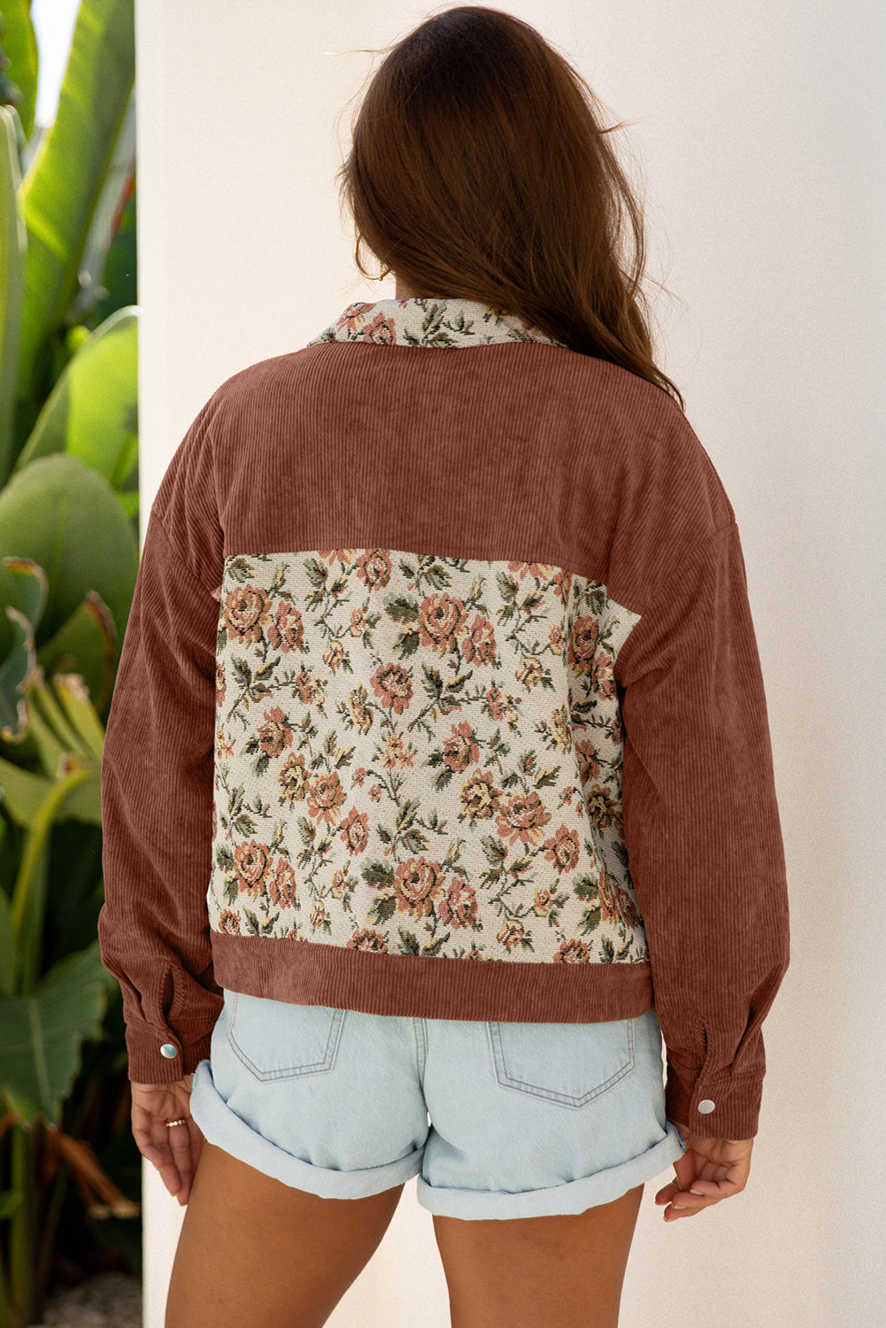 Person wearing a brown jacket with floral back panel against a white background