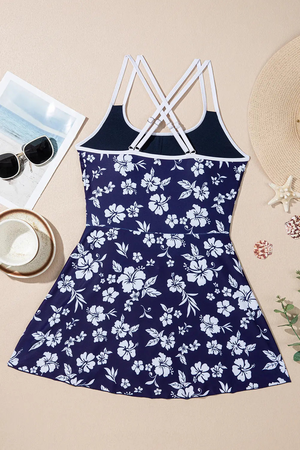 Navy blue dress with white floral pattern on a beige surface with sunglasses and a hat.