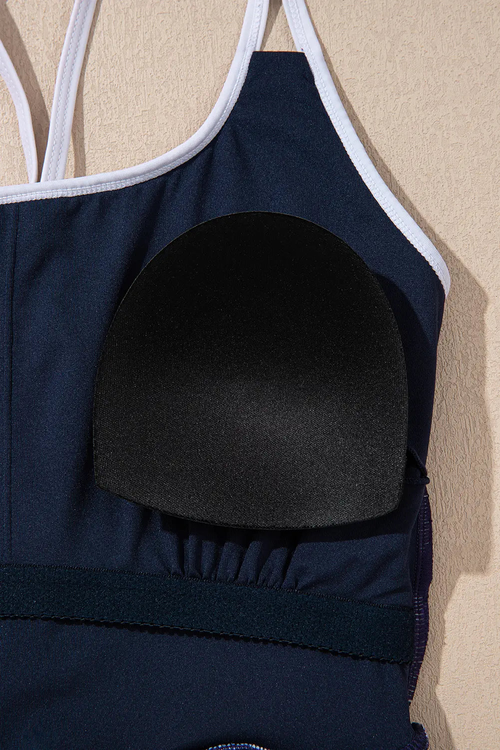 Navy blue swimsuit with white straps on a beige background