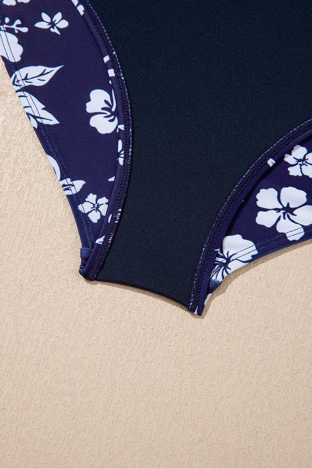 Navy swimsuit with white floral pattern on a beige background