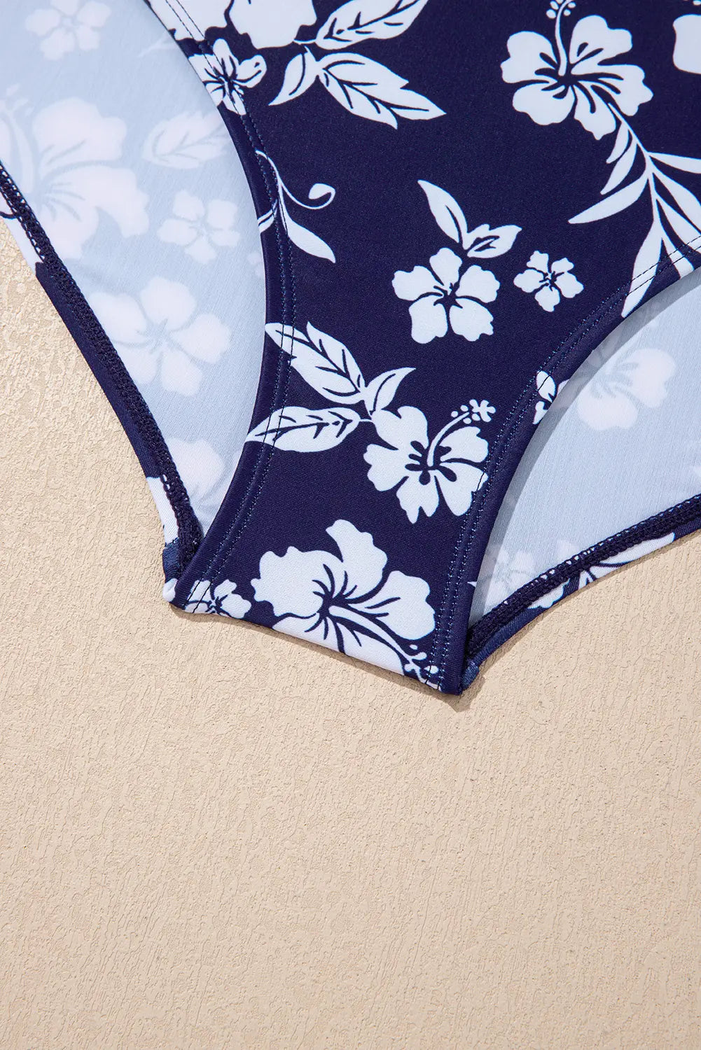 Navy blue swimsuit with white floral pattern on a beige background