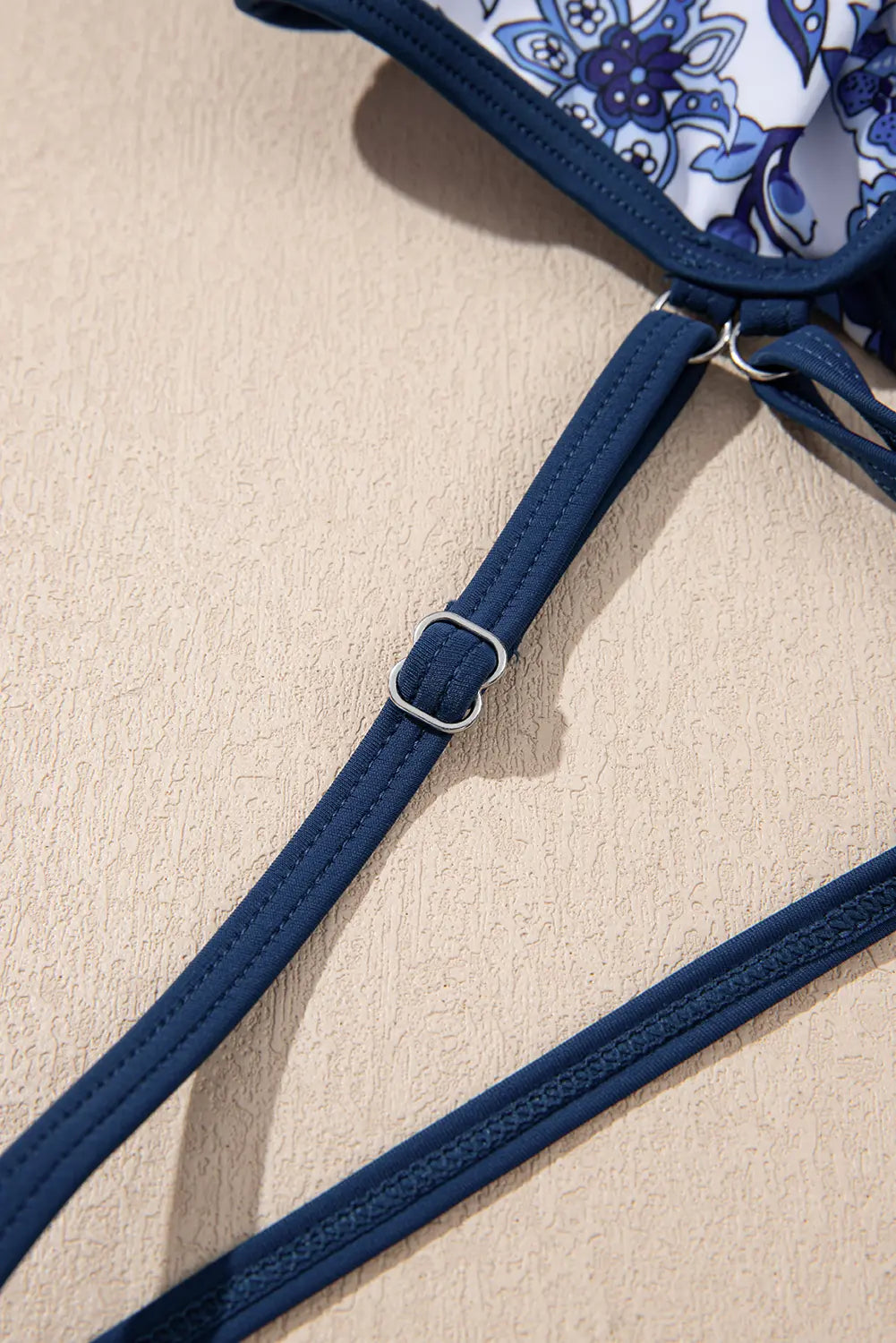 Close-up of a blue bikini strap on a beige surface
