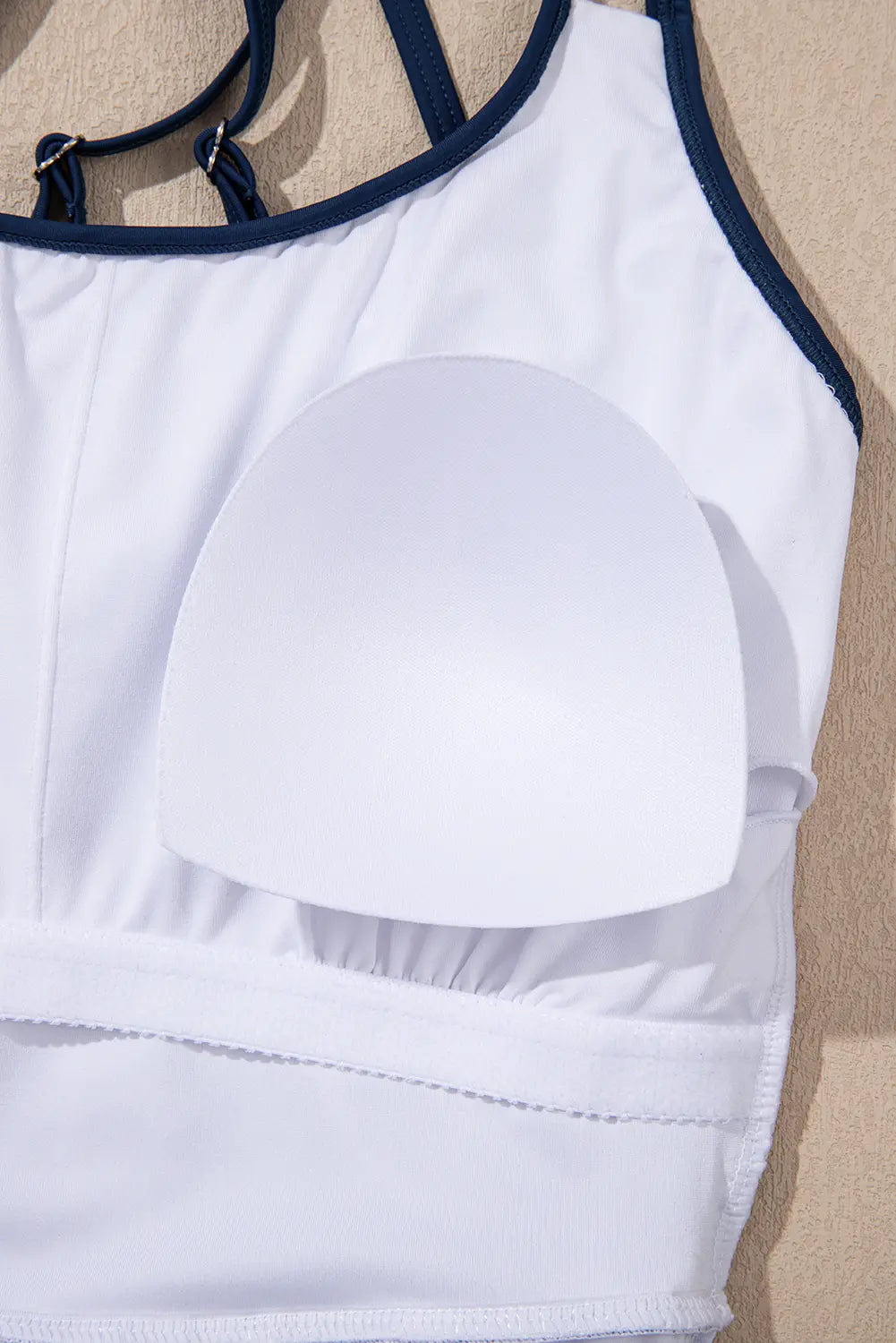 White sports bra with dark navy straps and trim, featuring a large white silicone or foam insert under the cup, shown against a neutral beige background.