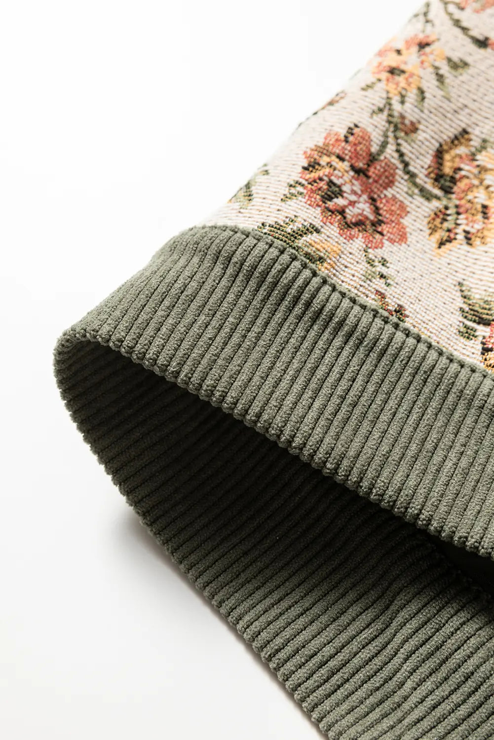 Close-up of a ribbed knit garment corner showing an olive green cuff meeting a cream floral patterned section with peach, pink, and green embroidery.