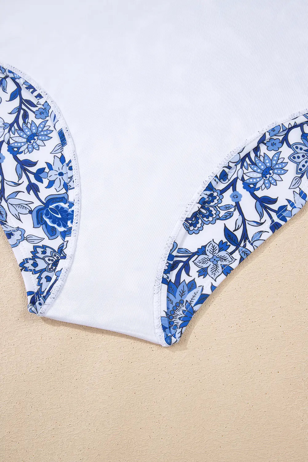White swimsuit top with blue floral patterns on a beige and white background