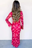 A woman viewed from behind wearing a long-sleeve, form-fitting maxi dress with a vibrant pink and red floral pattern. She is holding a small red clutch against a plain white wall and gray floor.