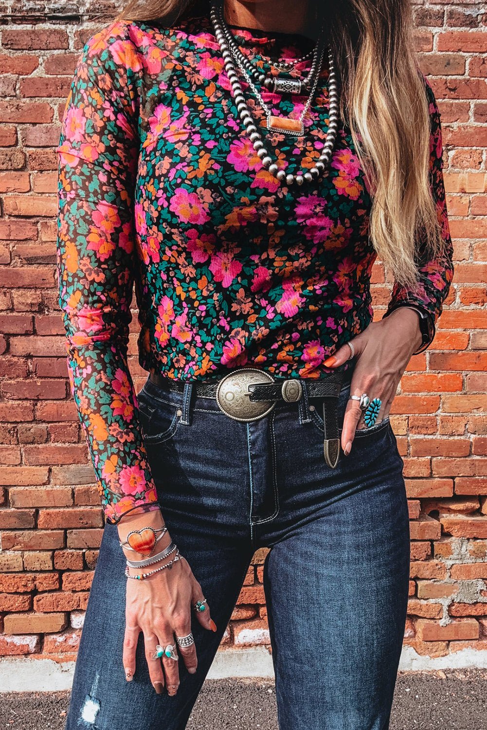 Person wearing a colorful floral top and blue jeans against a brick wall.