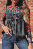 Woman wearing a floral long-sleeve top over a plaid dress with denim jeans against a brick wall.