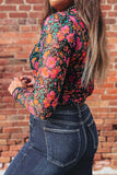 Person wearing a colorful floral long-sleeve top and blue jeans against a brick wall.