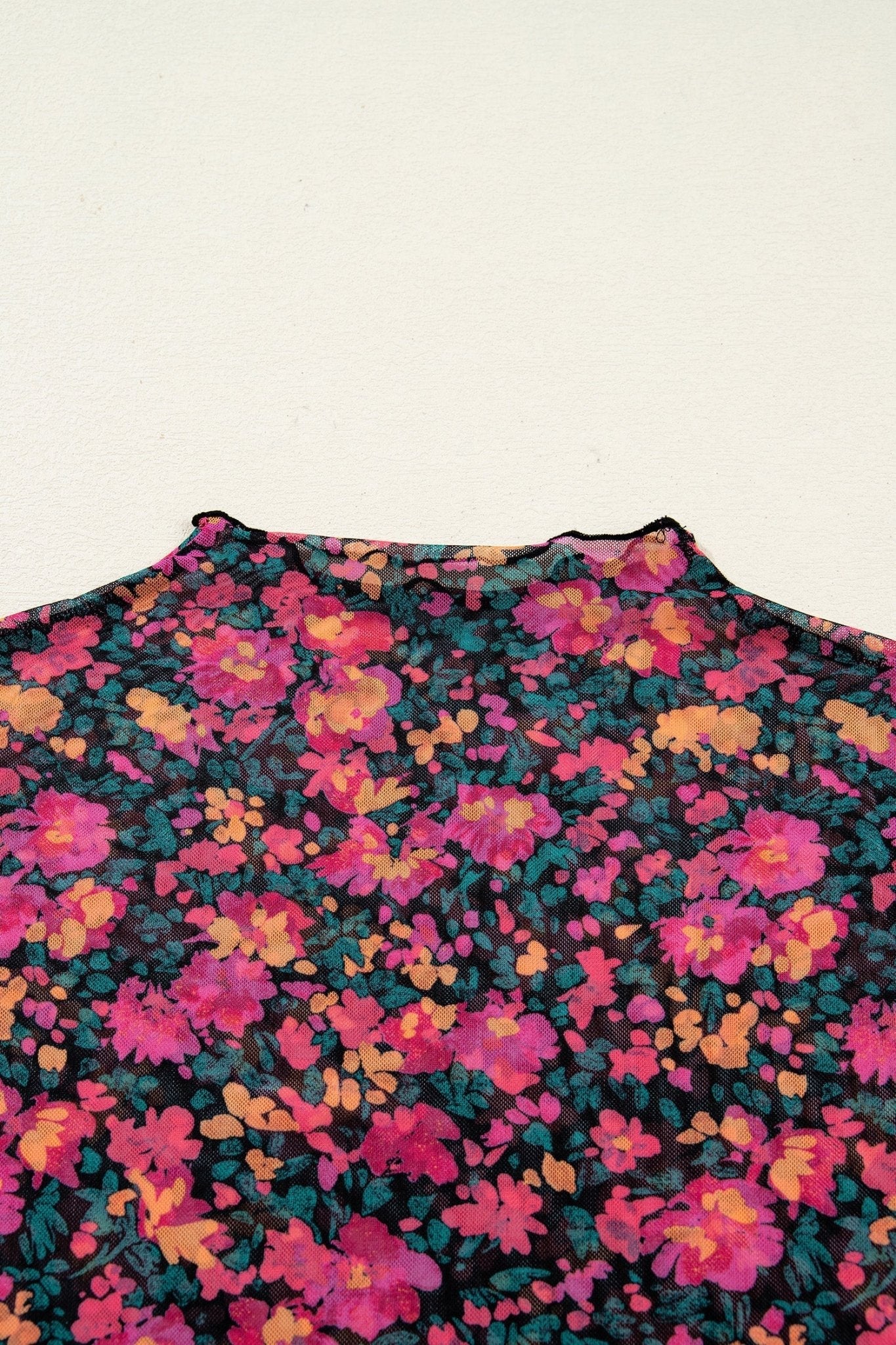 Close-up of a floral patterned fabric with pink, purple, and green colors on a beige background.