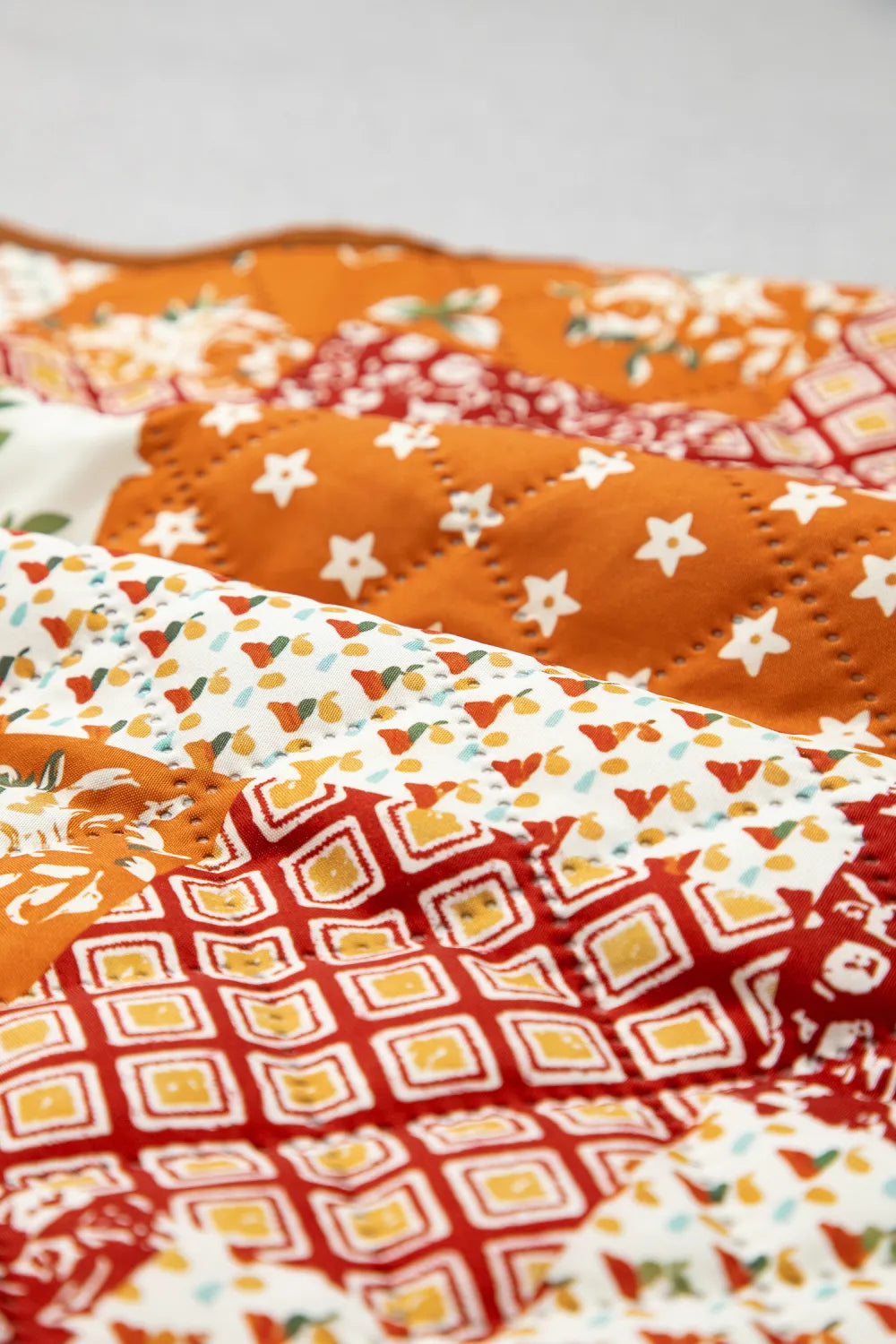 Close-up of quilted fabric with orange star, red geometric, and white multicolored patterned sections.