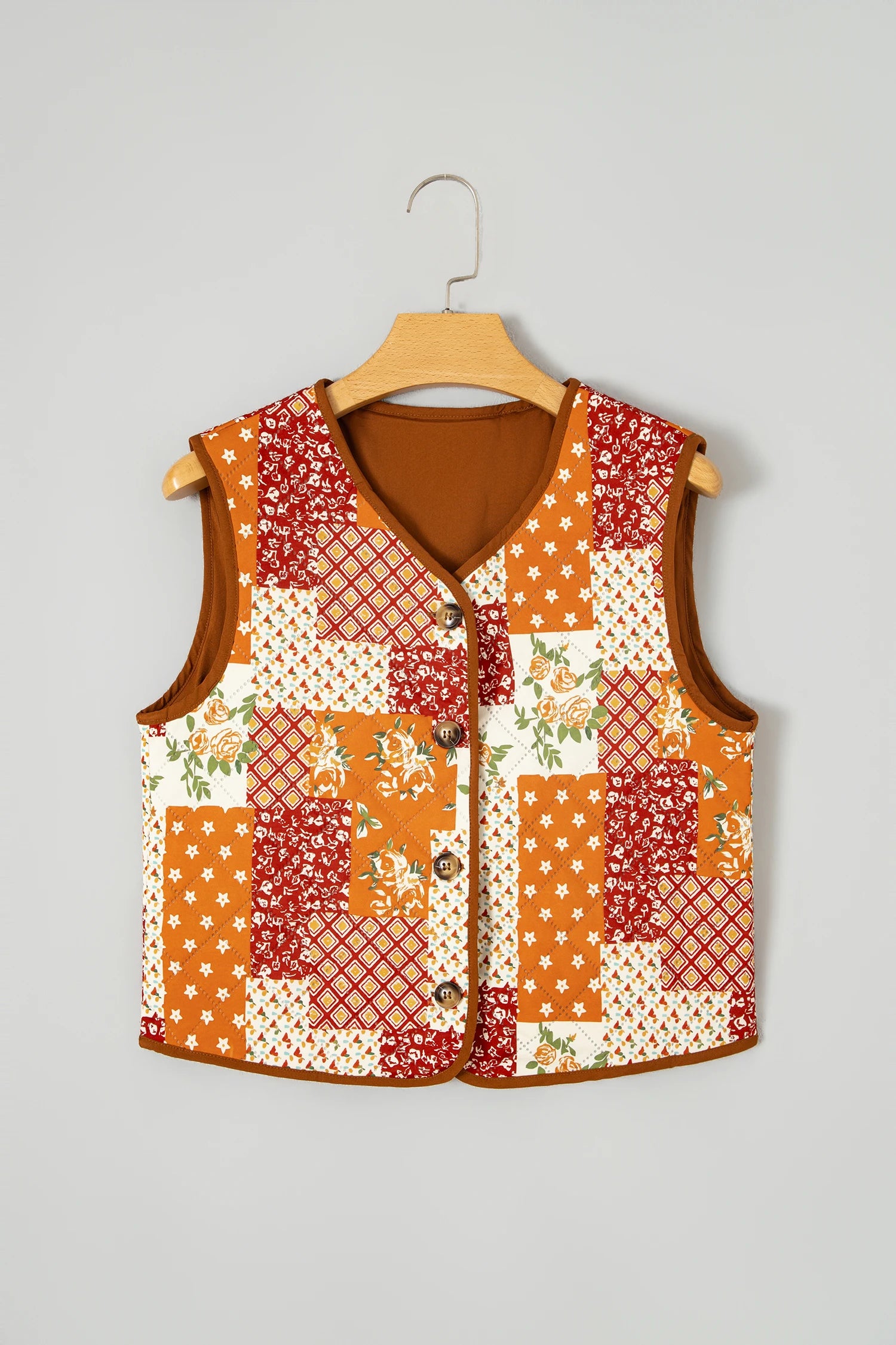 Sleeveless patchwork vest with orange, red, and cream floral patterns hanging on a wooden hanger.