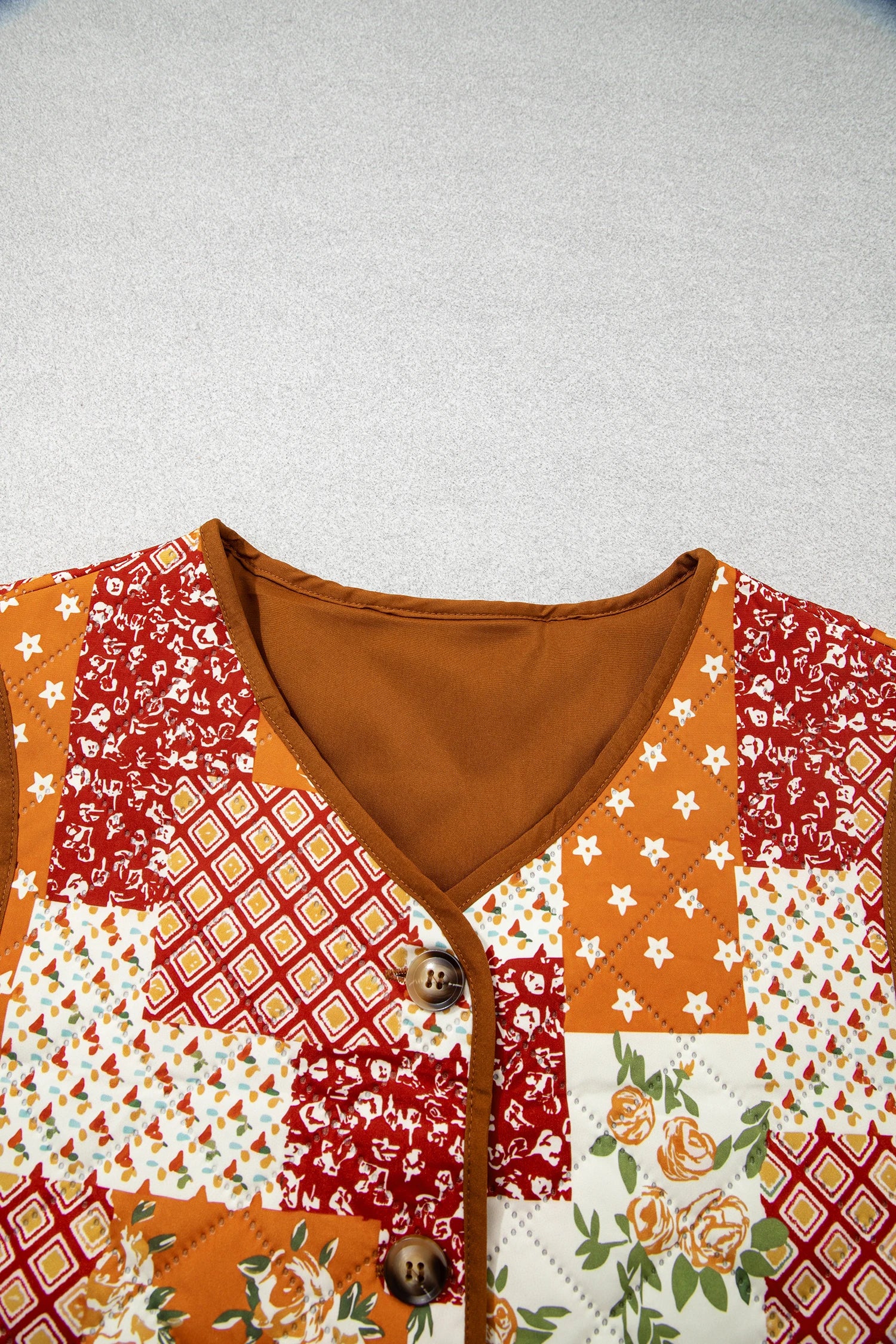 Close-up of patchwork quilted cardigan with V-neck, orange, red, white patterns, and brown buttons.