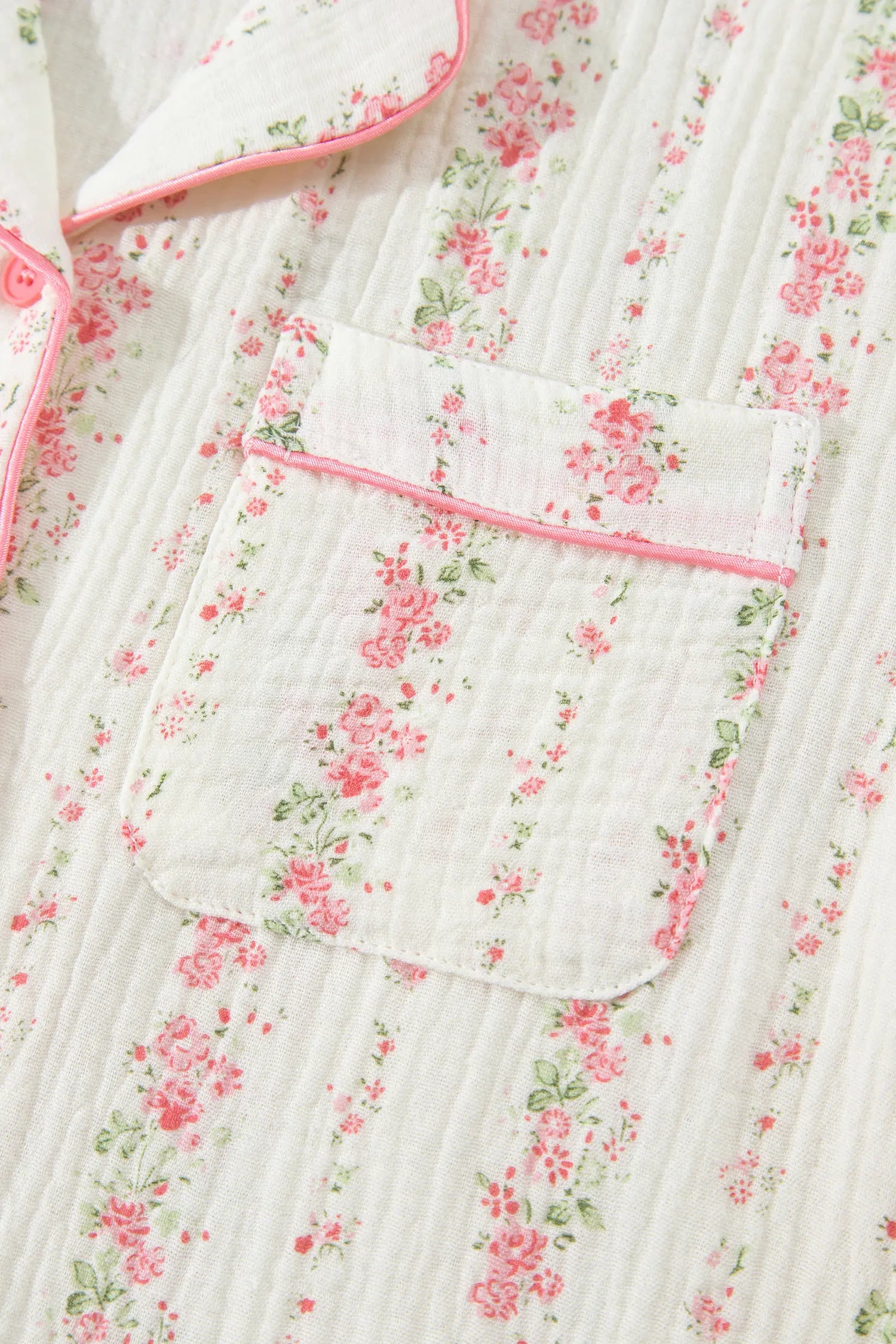 Close-up of white muslin pajamas with pink-green floral print and pink-trimmed pocket.