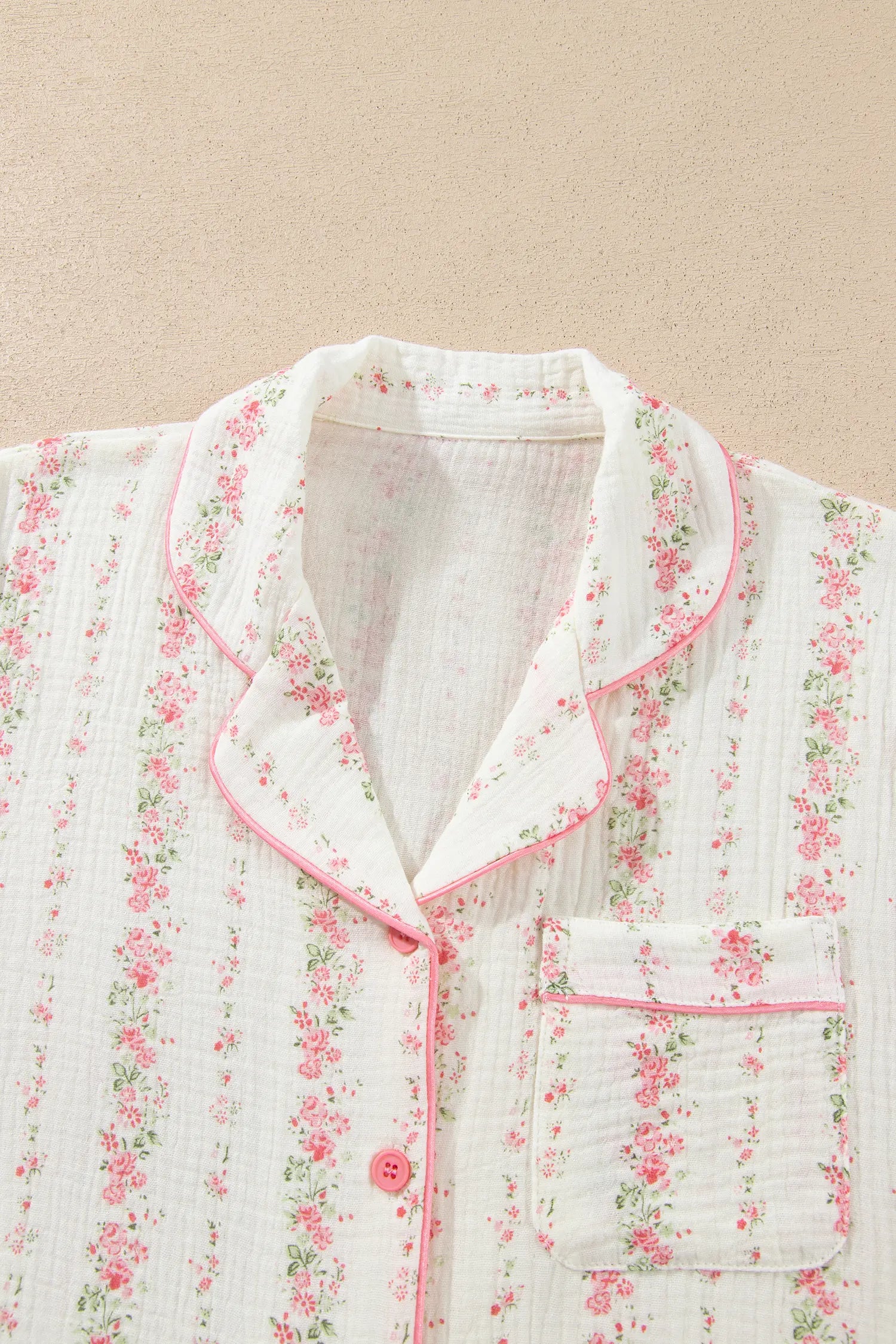 Close-up of white muslin pajama shirt with pink-green floral print and pink piping.