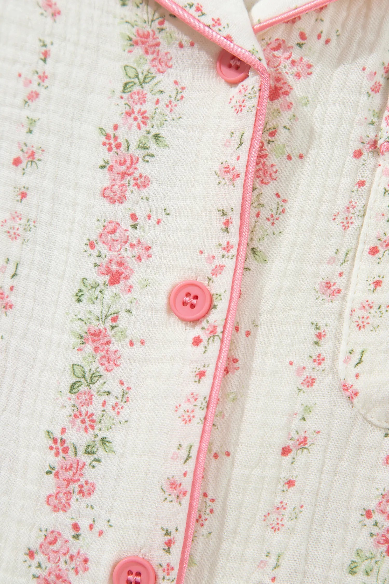 Close-up of white muslin shirt with pink-green floral print and pink piping.