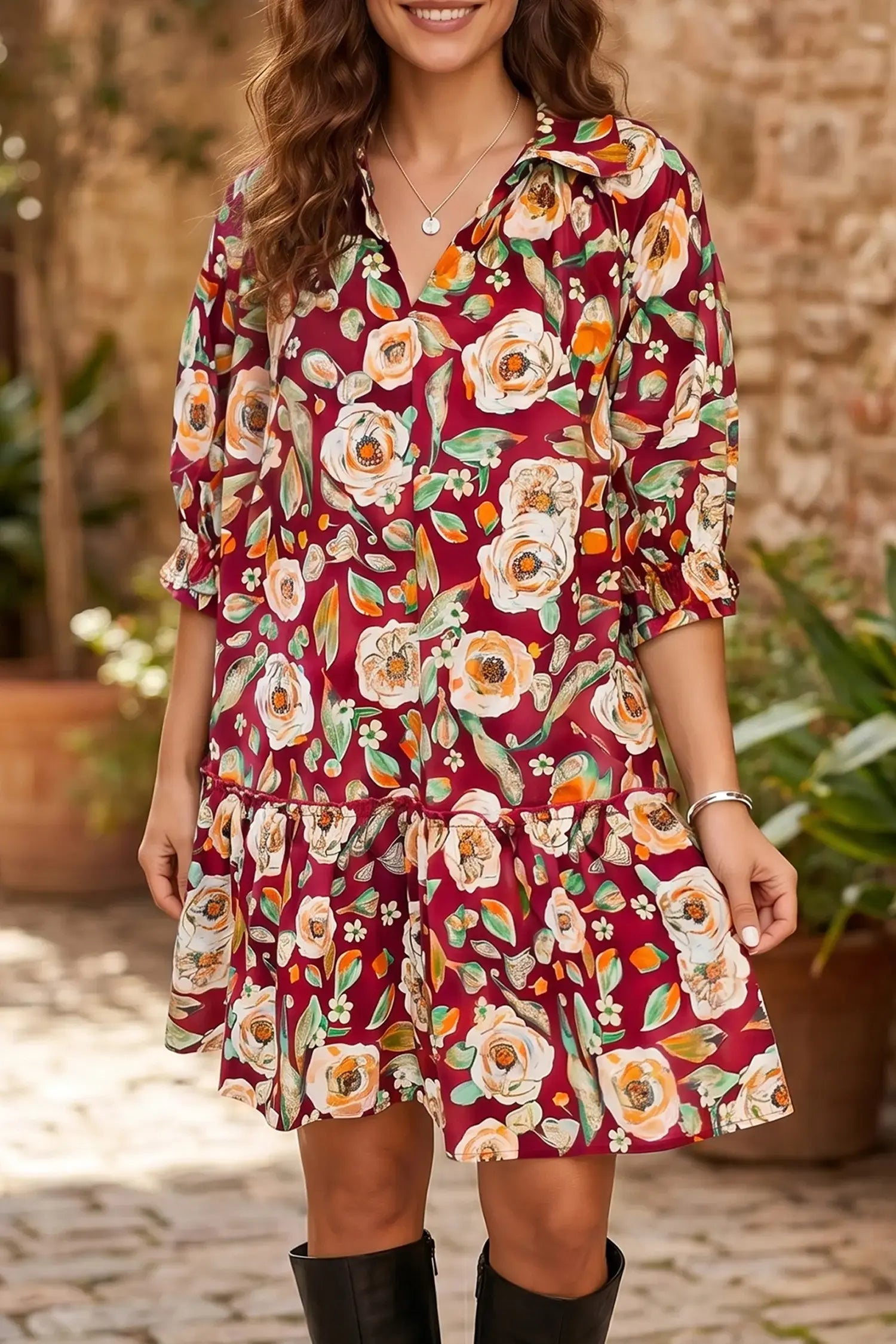 A woman wearing a short-sleeve collared dress with a red base and a large floral print in cream, orange, and green, paired with black boots in an outdoor setting.