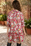 A woman viewed from behind wearing a red tiered shirt dress with a colorful floral print, standing on a cobblestone patio with potted plants and a brick wall in the background.