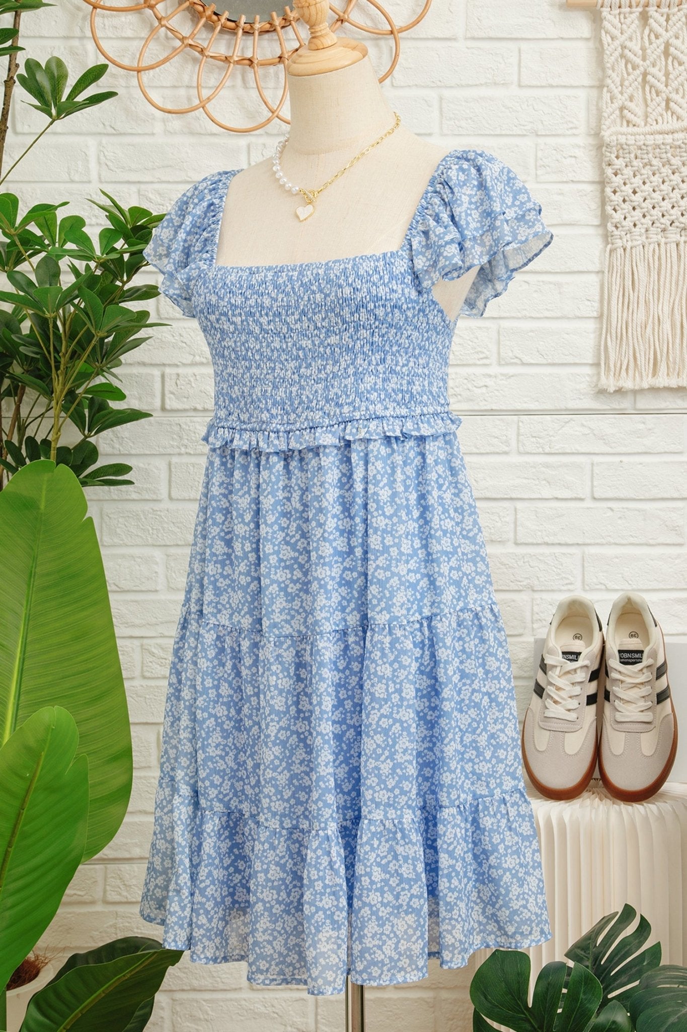 Blue floral dress on a mannequin with sneakers beside it against a white brick wall.
