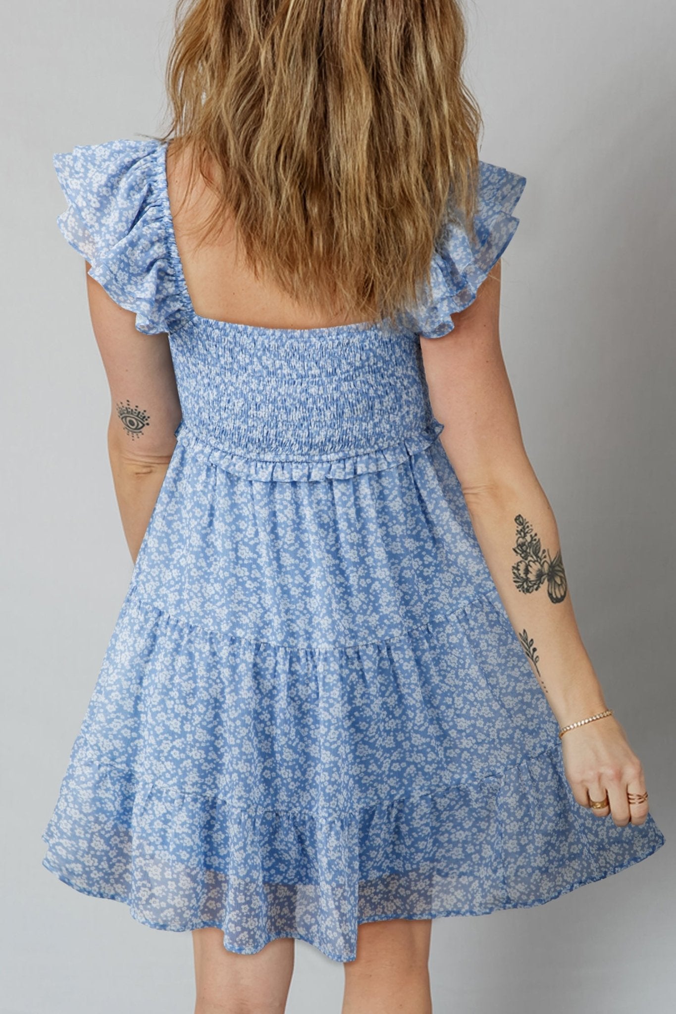 Blue floral dress worn by a person with tattoos on a gray background