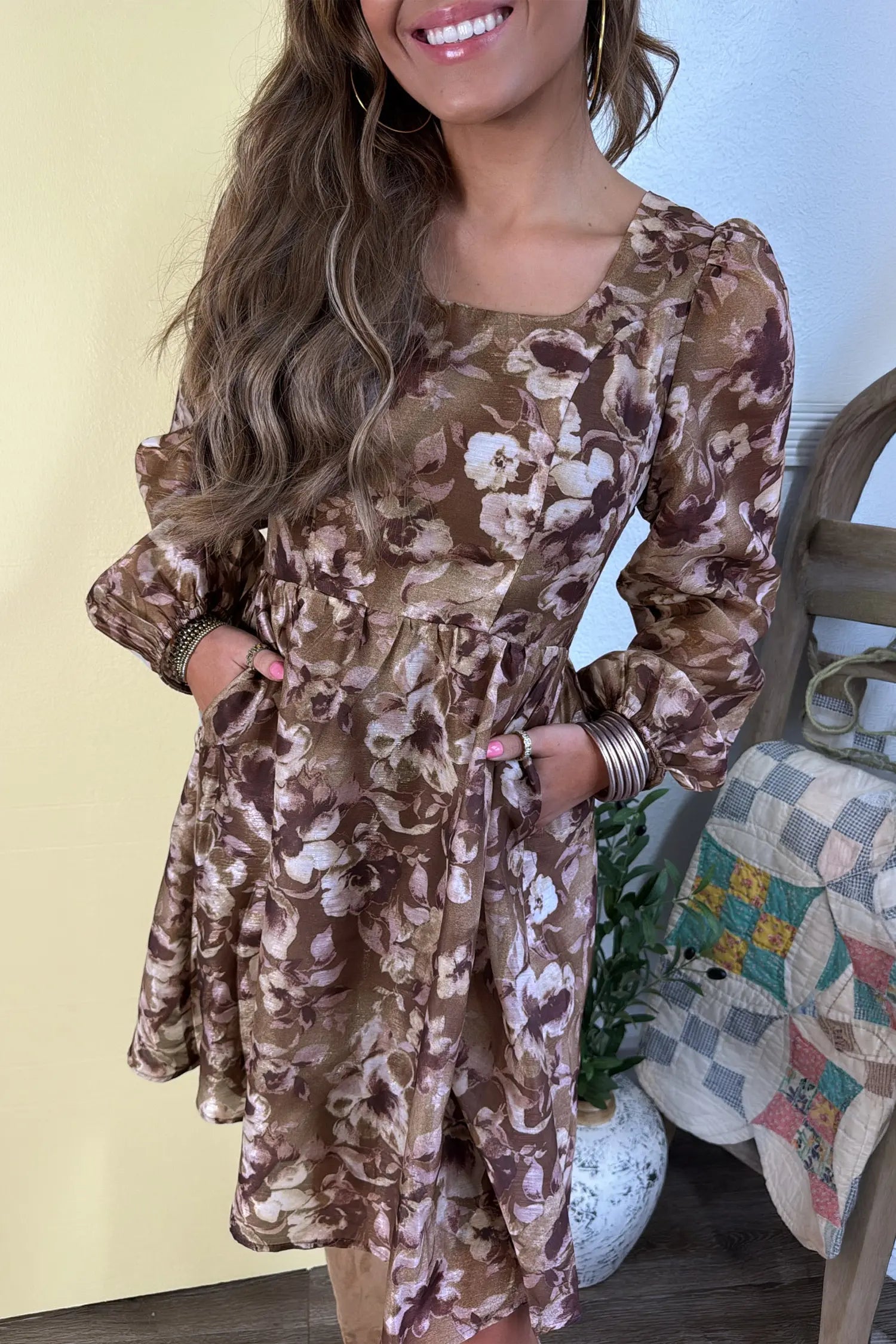 A woman wearing a brown and beige floral print long-sleeve dress with a square neckline and ruffled sleeves, standing in an indoor setting.