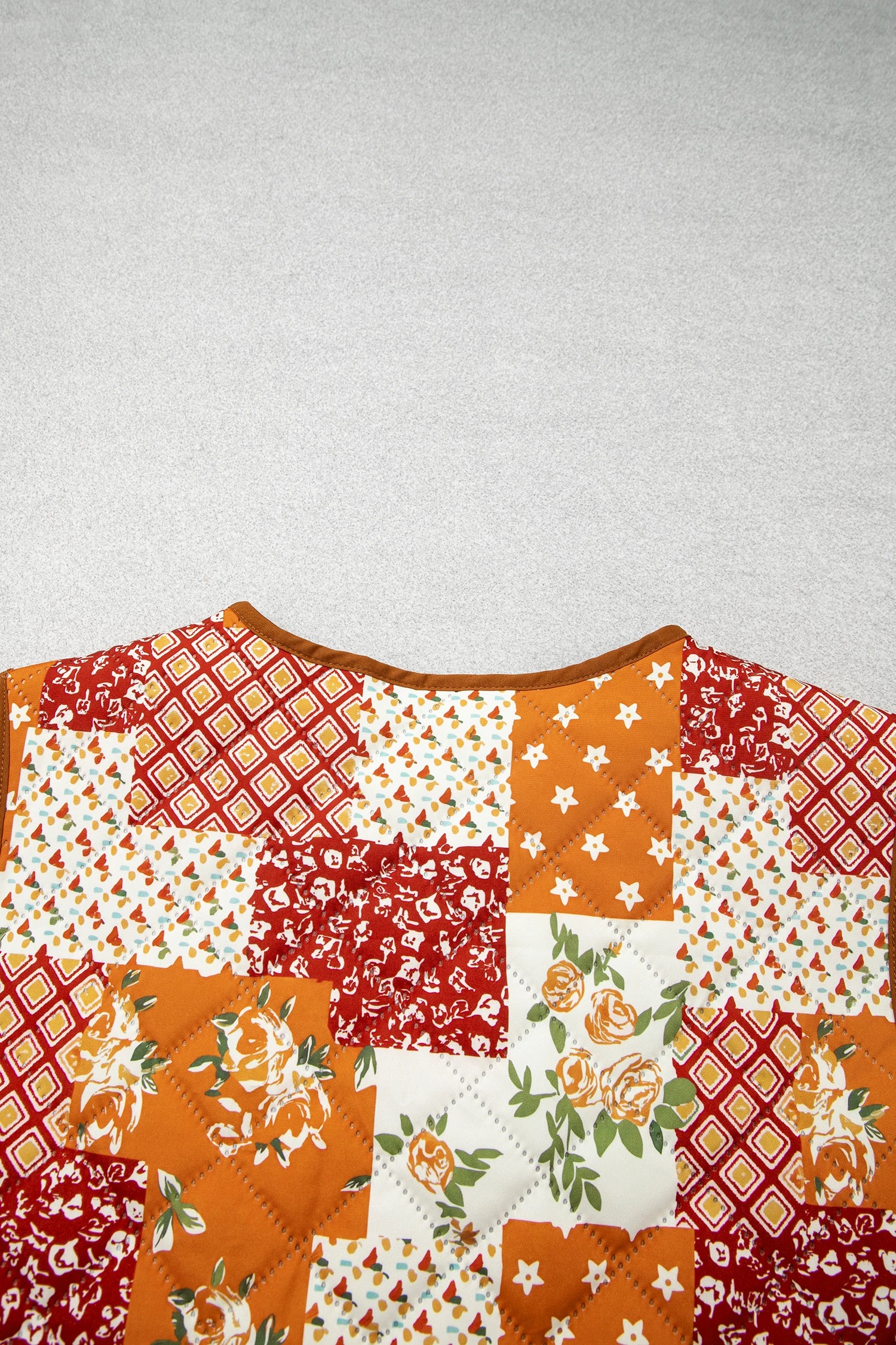 Close-up of quilted patchwork top with orange, red, white floral and geometric squares.
