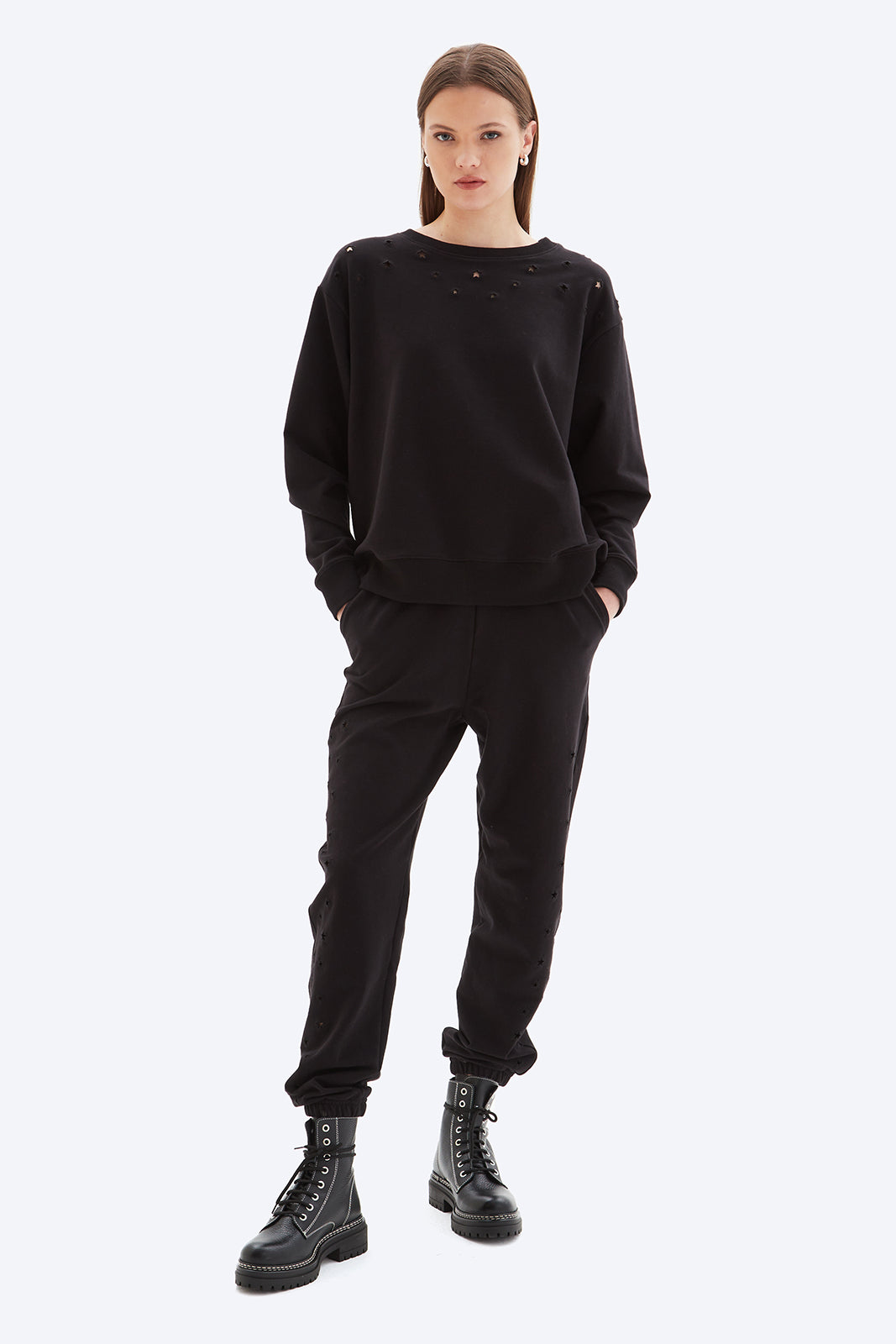 Person wearing a black outfit with black boots on a white background