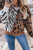 A woman wearing a fuzzy knit sweater with a color-blocked animal print design featuring zebra stripes on the left, leopard print on the right, and a solid brown ribbed hem, paired with blue jeans and layered pearl necklaces.