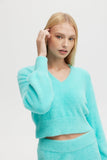 Woman wearing a turquoise sweater and pants on a light gray background