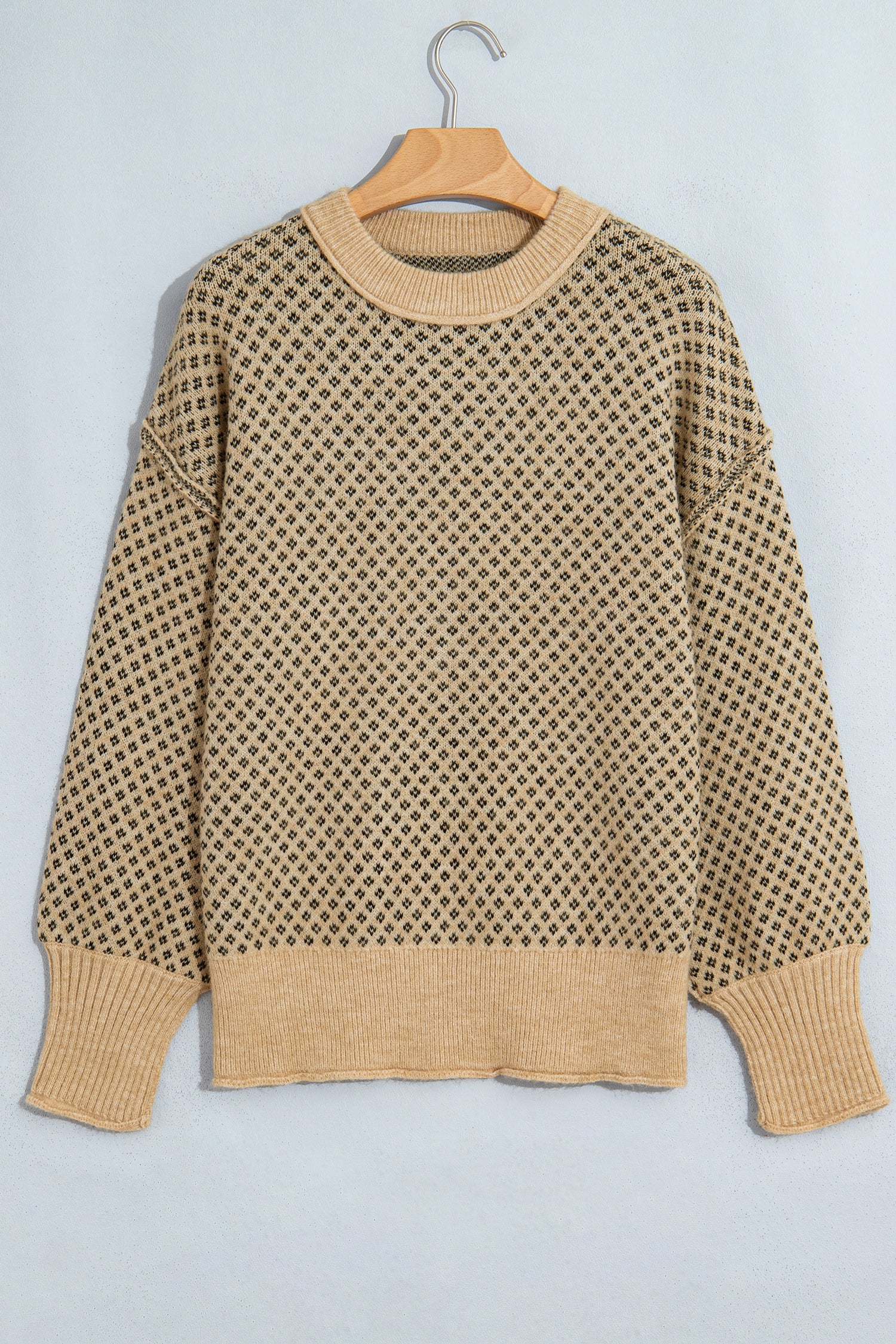 A beige and brown knit sweater with a geometric pattern, hanging on a wooden hanger against a light gray background.