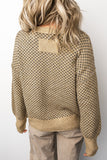 Person wearing a patterned beige sweater and light-colored pants on a plain background