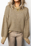 Person wearing a patterned beige sweater and light-colored pants against a plain background