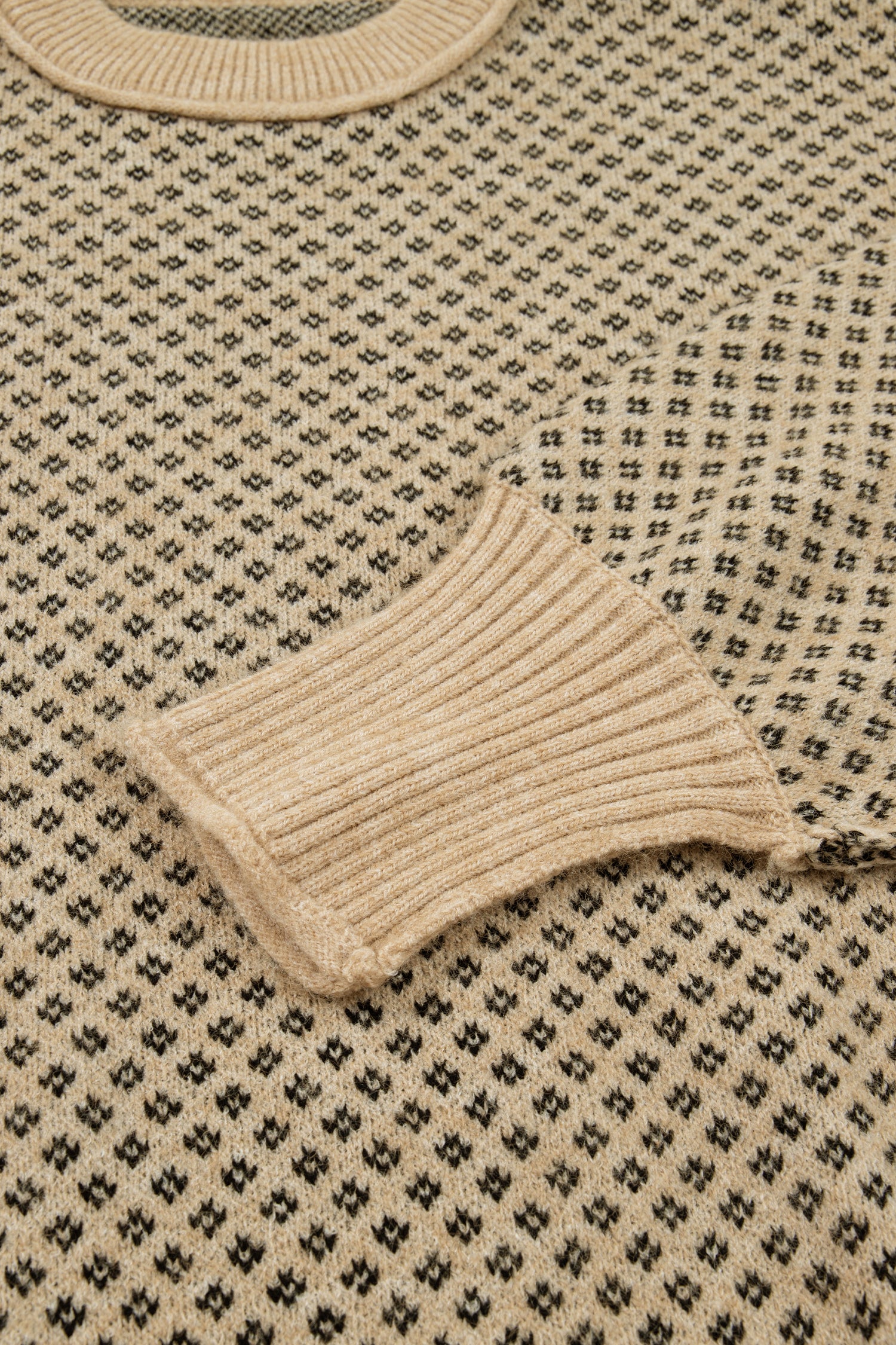 Close-up of a beige knit sweater with a black geometric pattern and ribbed collar and cuff.
